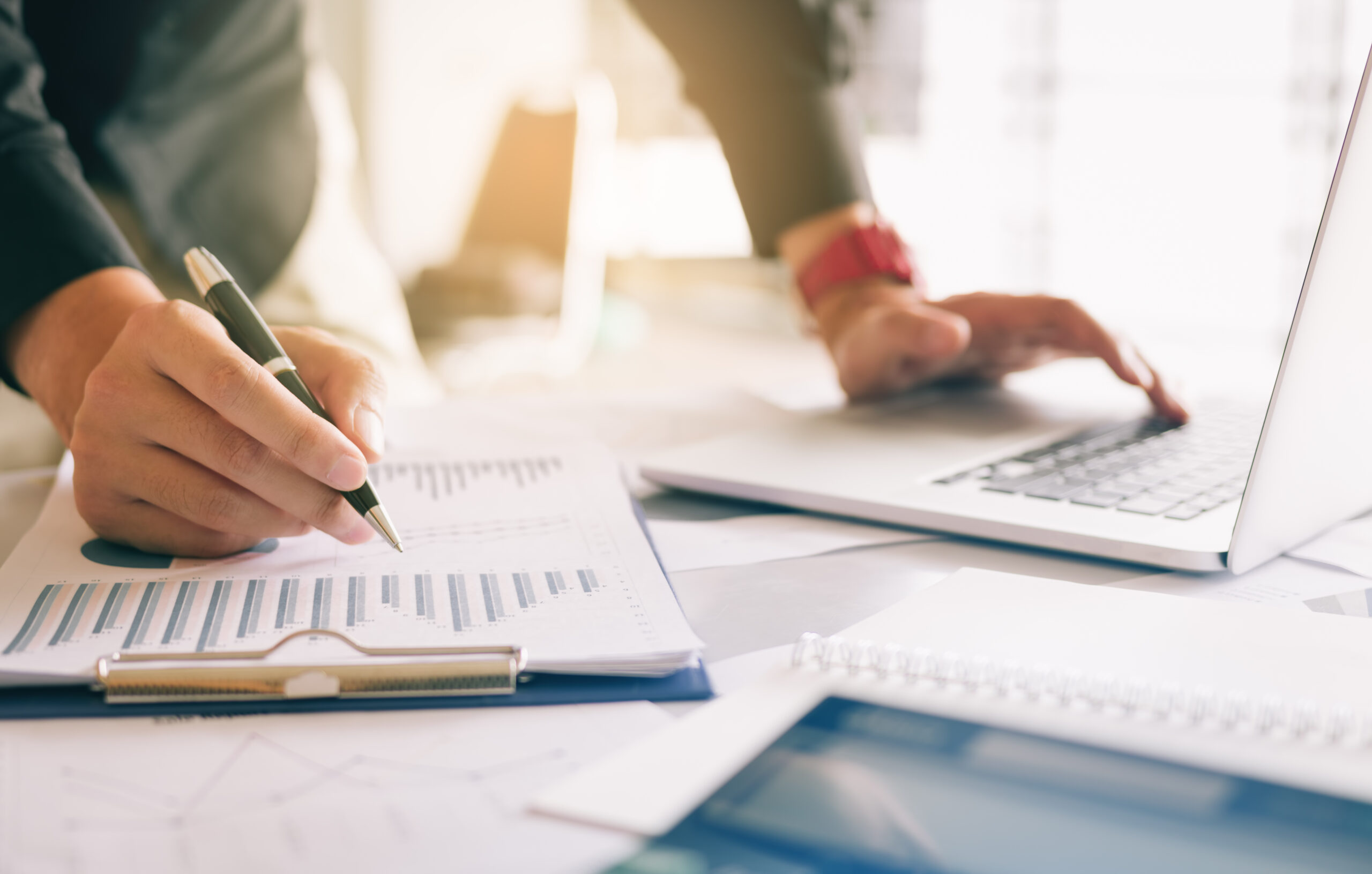 Personne tenant un stylo et pointant un résumé du tableau en papier analysant le rapport d’activité annuel avec l’utilisation d’un ordinateur portable au bureau de la chambre.