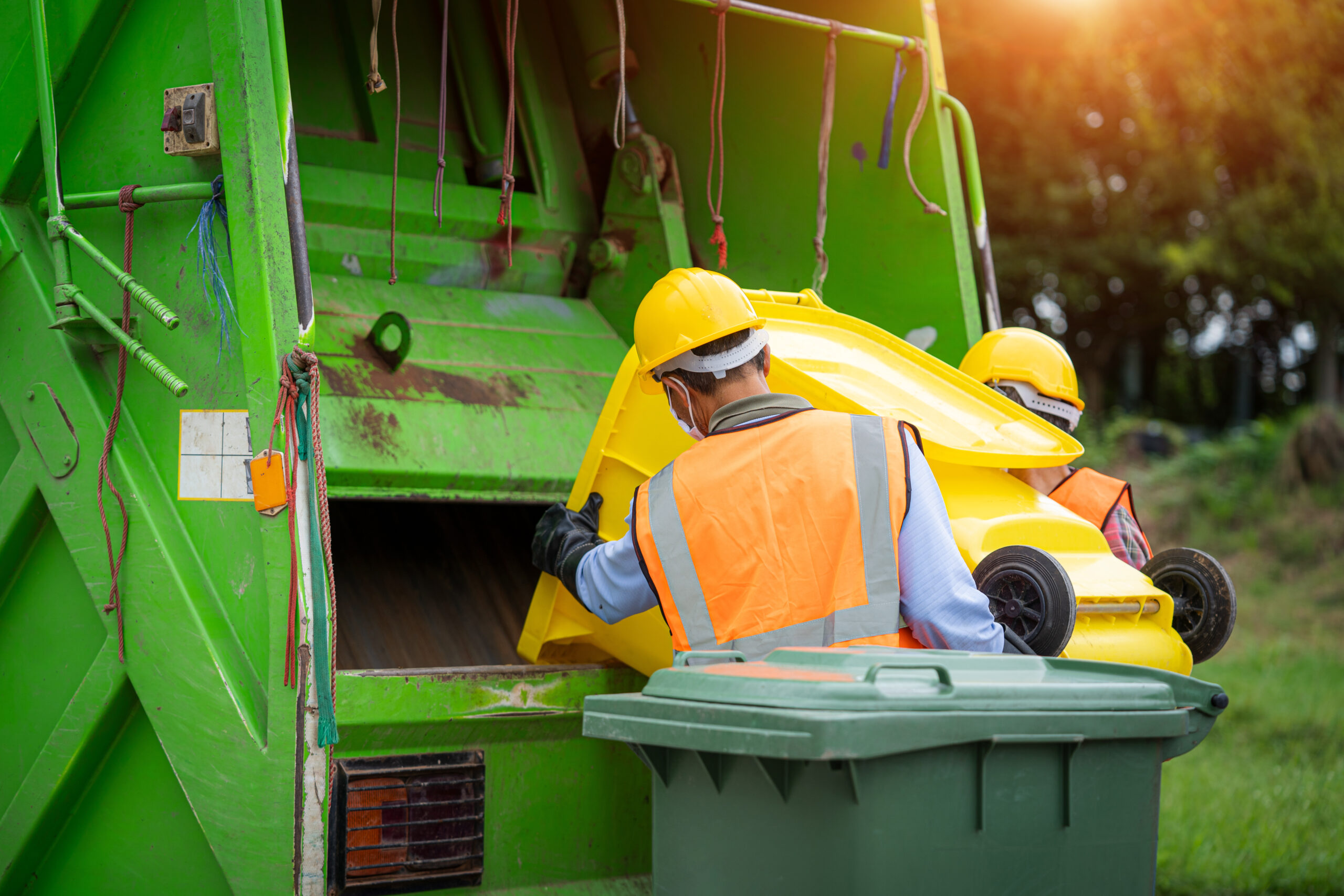 Agent travaillant avec un camion à ordures vert chargeant des déchets et une poubelle à la ville, collecteurs de déchets au travail.